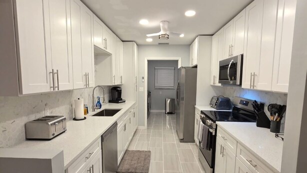 A modern kitchen with white cabinets, stainless steel appliances, and a tiled floor. - Pleasant 3-bedroom house with pool in peaceful setting (Naples)