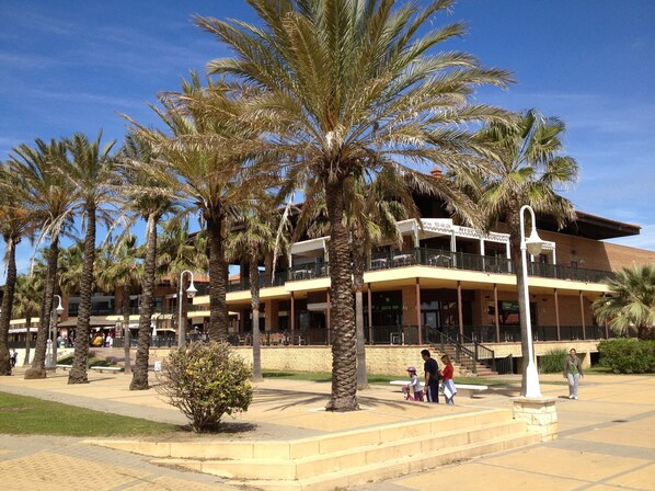 A building with multiple floors, outdoor seating, and palm trees.