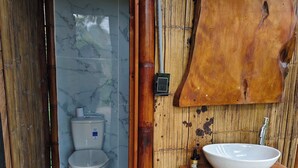 Un bany amb vàter, un lavabo de fusta i una paret de bambú.