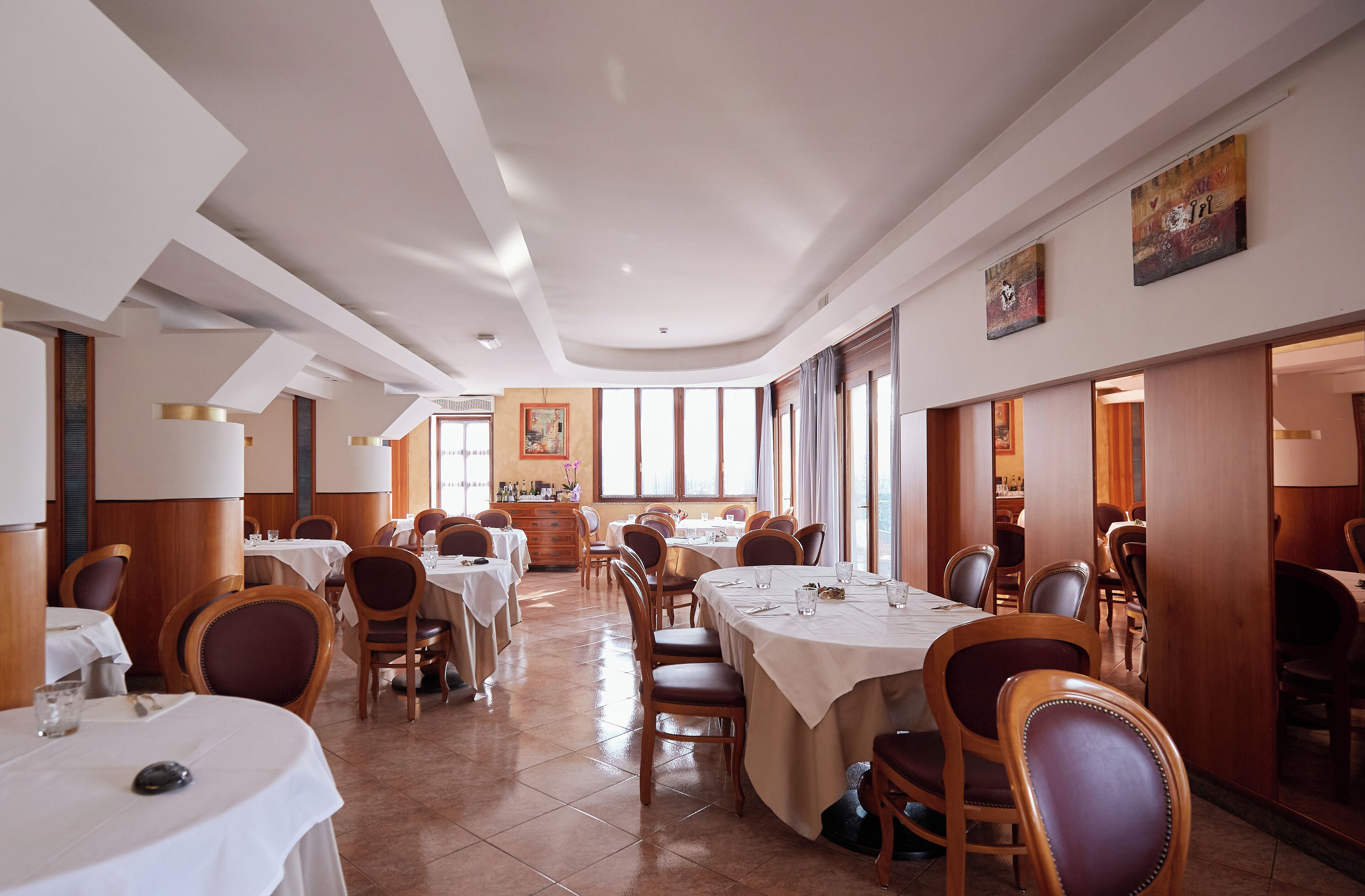 A spacious dining area with multiple tables and chairs, large windows, and a modern ceiling design.