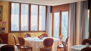 A dining area with a round table set for six, wooden chairs, and a view through large windows. - Albergo Ristorante Belvedere (Codroipo)
