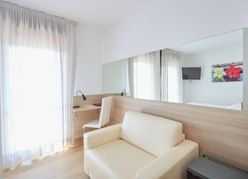 Una habitación de hotel moderna con una cama grande, un escritorio con silla, un televisor de pantalla plana y un espejo amplio.