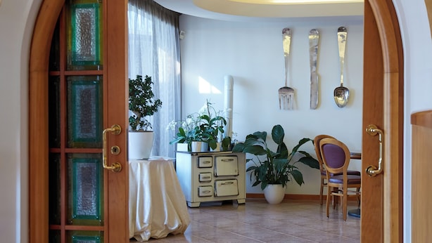 An interior view of a room with a wooden door, a potted plant, a table with a white tablecloth, a dresser, and a chair. - Albergo Ristorante Belvedere (Codroipo)