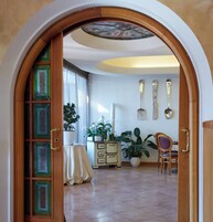 Vista interior de una habitación con puerta de madera, planta en maceta, mesa con mantel blanco, cómoda y una silla.