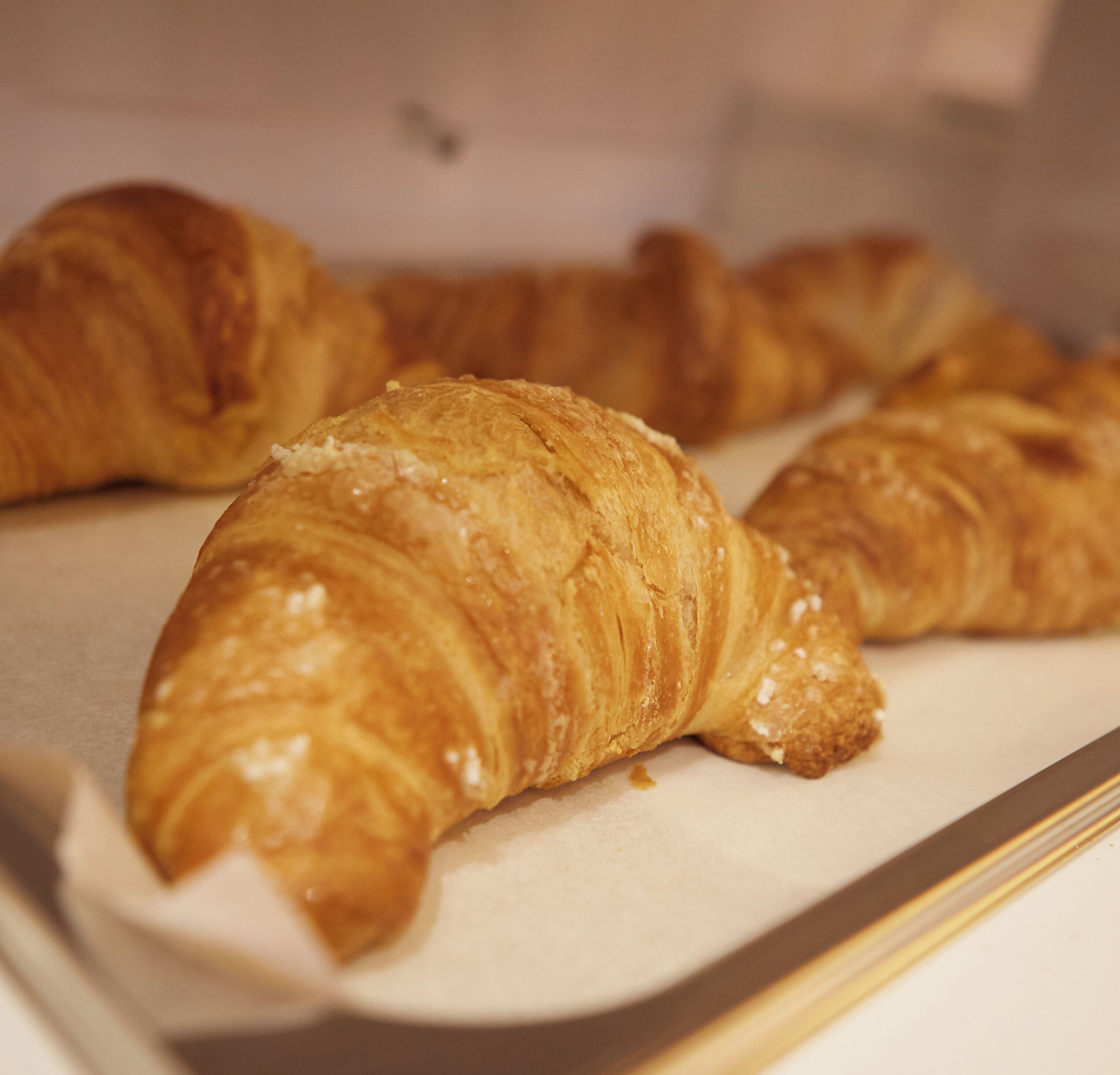 Une plaque de croissants dorés et brillants, probablement fraîchement sortis du four, présentés sur une feuille de papier blanc.
