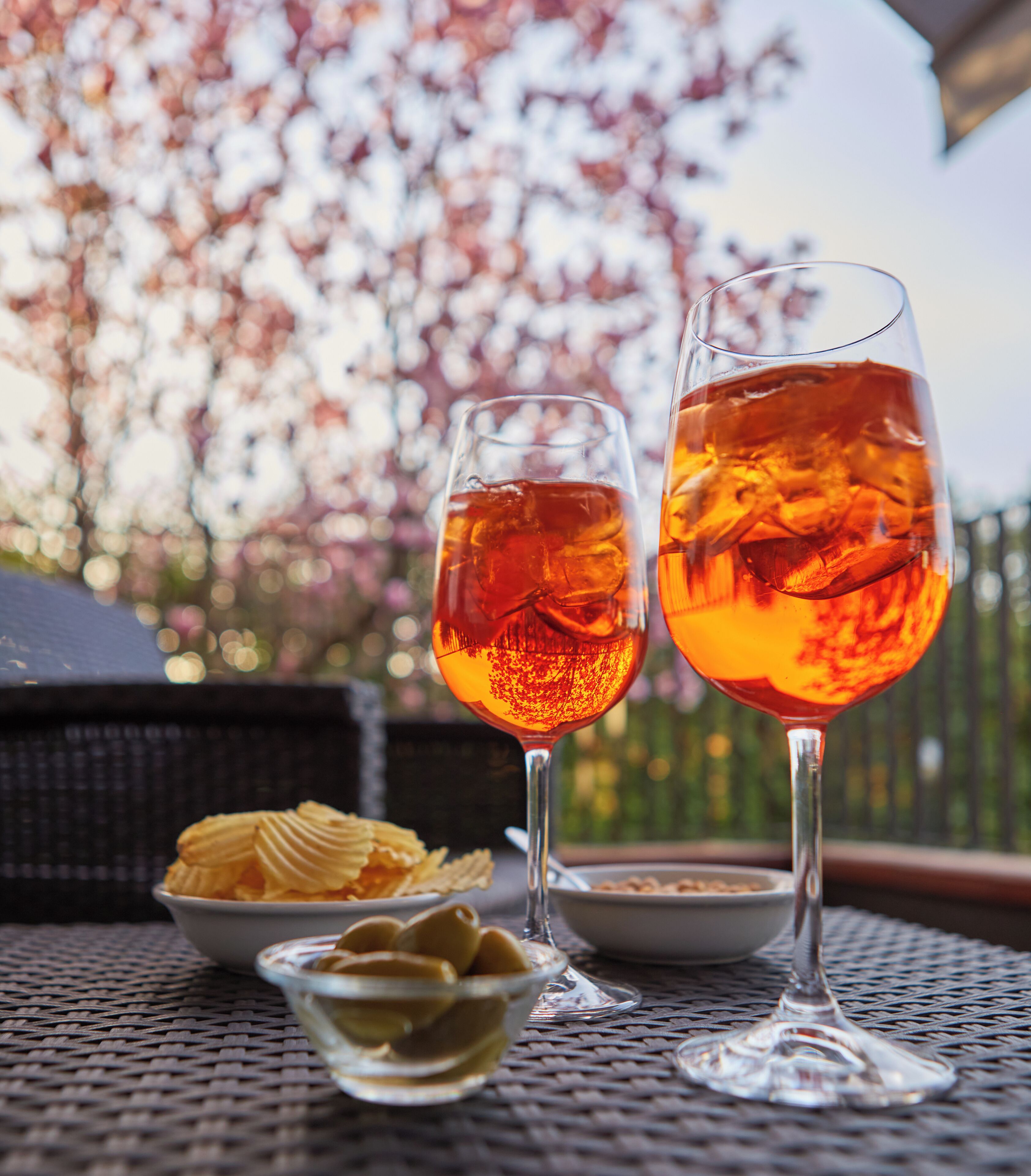 Dos vasos de una bebida de color ámbar sobre una mesa con un tazón de papas fritas y aceitunas.