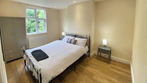 A bedroom with a bed, a nightstand, a wardrobe, and a window. - Mayfield Escape - Stylish Two Bed Apartment (South Croydon)