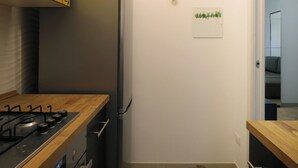 Una cocina compacta de diseño moderno, con un refrigerador de acero inoxidable, una encimera de madera y un pequeño ventanal con paneles de vidrio esmerilado.