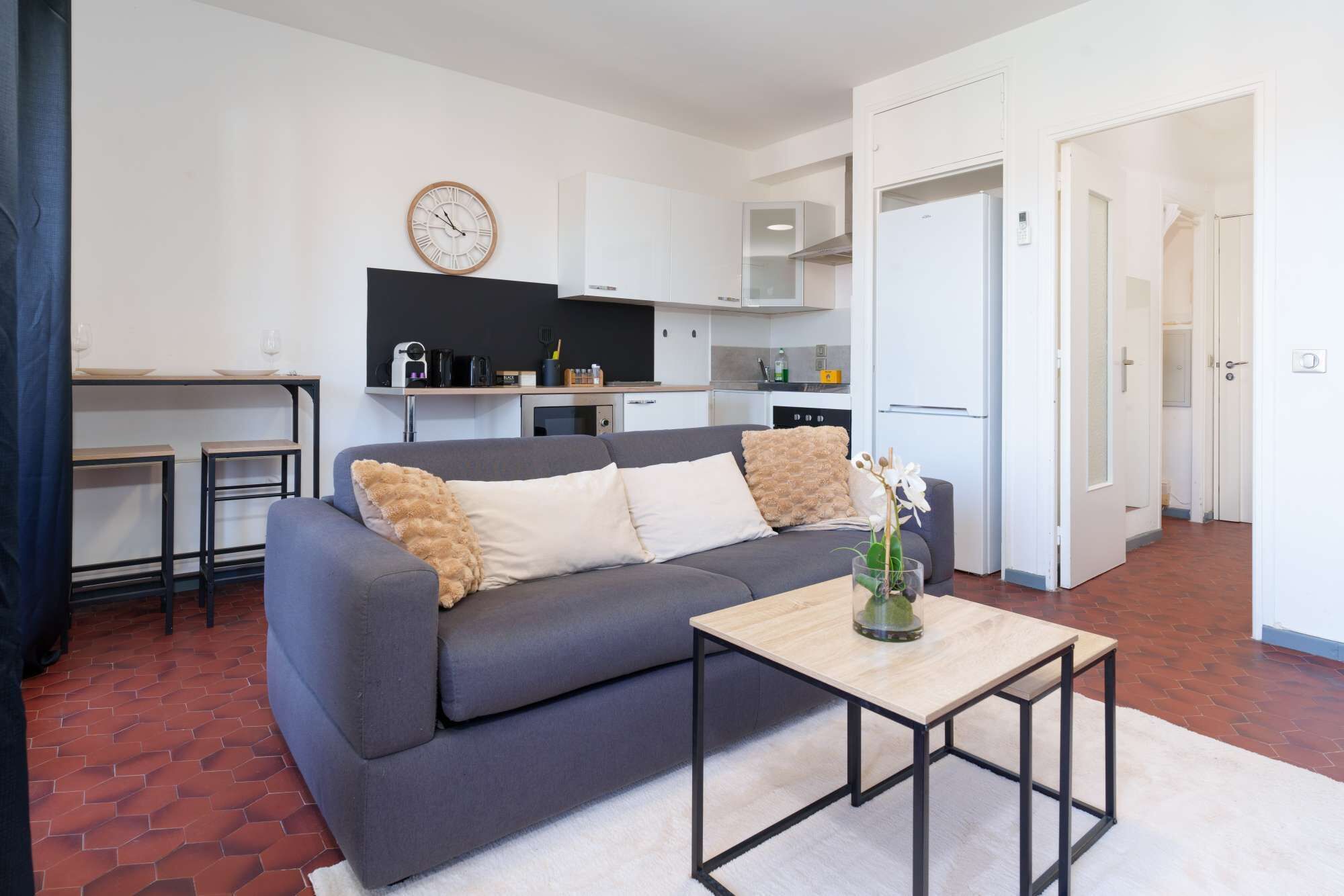 A modern living room with a grey sofa, a small wooden coffee table, and a kitchen area in the background.