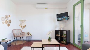 Un salon comprenant un canapé, un fauteuil, une petite table, un téléviseur et une bibliothèque.