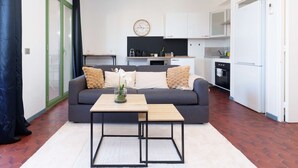 Un espace de vie compact comprenant un canapé, une table basse et un coin cuisine équipé d’un réfrigérateur, d’un four et d’un four à micro-ondes.