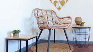 Une pièce comprenant un fauteuil en rotin, une petite table, une décoration murale en macramé et une autre décoration murale en macramé représentant des motifs en forme de cœur.