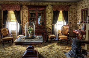 Quarto antigo com um armário de madeira, duas cadeiras, uma mesa com cúpula de vidro e um fogão antigo.