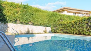 Ein klares Schwimmbecken mit einer Metallleiter, umgeben von einer Steinmauer und üppiger Vegetation.