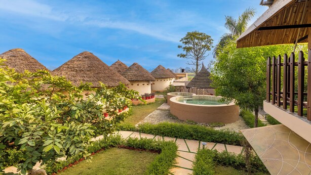 Un patio con construcciones de techo de paja, una piscina y abundante vegetación.