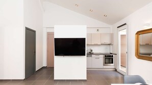 Una cuina moderna amb televisió de pantalla plana, una zona de menjador amb taula i cadires, i un mirall gran a la paret.