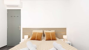 Habitació d'hotel amb un llit, dos coixins, una taula de nit amb una làmpada i una porta gris.