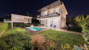 Una casa moderna de dos pisos con piscina, mobiliario exterior y un jardín bien cuidado.