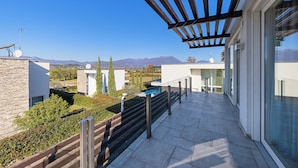 Un balcón moderno al aire libre con una pérgola, paredes de piedra y vistas a montañas.