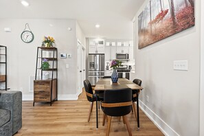 A modern kitchen with white cabinets, stainless steel appliances, and a dining area with a wooden table and black chairs. - Modern Durham retreat / 10 mins from Duke and downtown Durham (Durham)