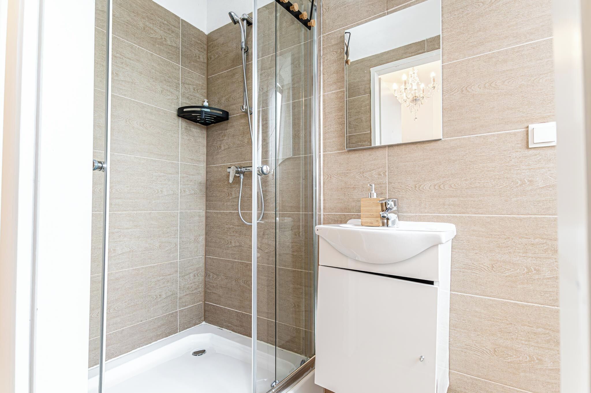 Une salle de bain moderne avec une douche à parois de verre, un lavabo blanc et un miroir au-dessus.