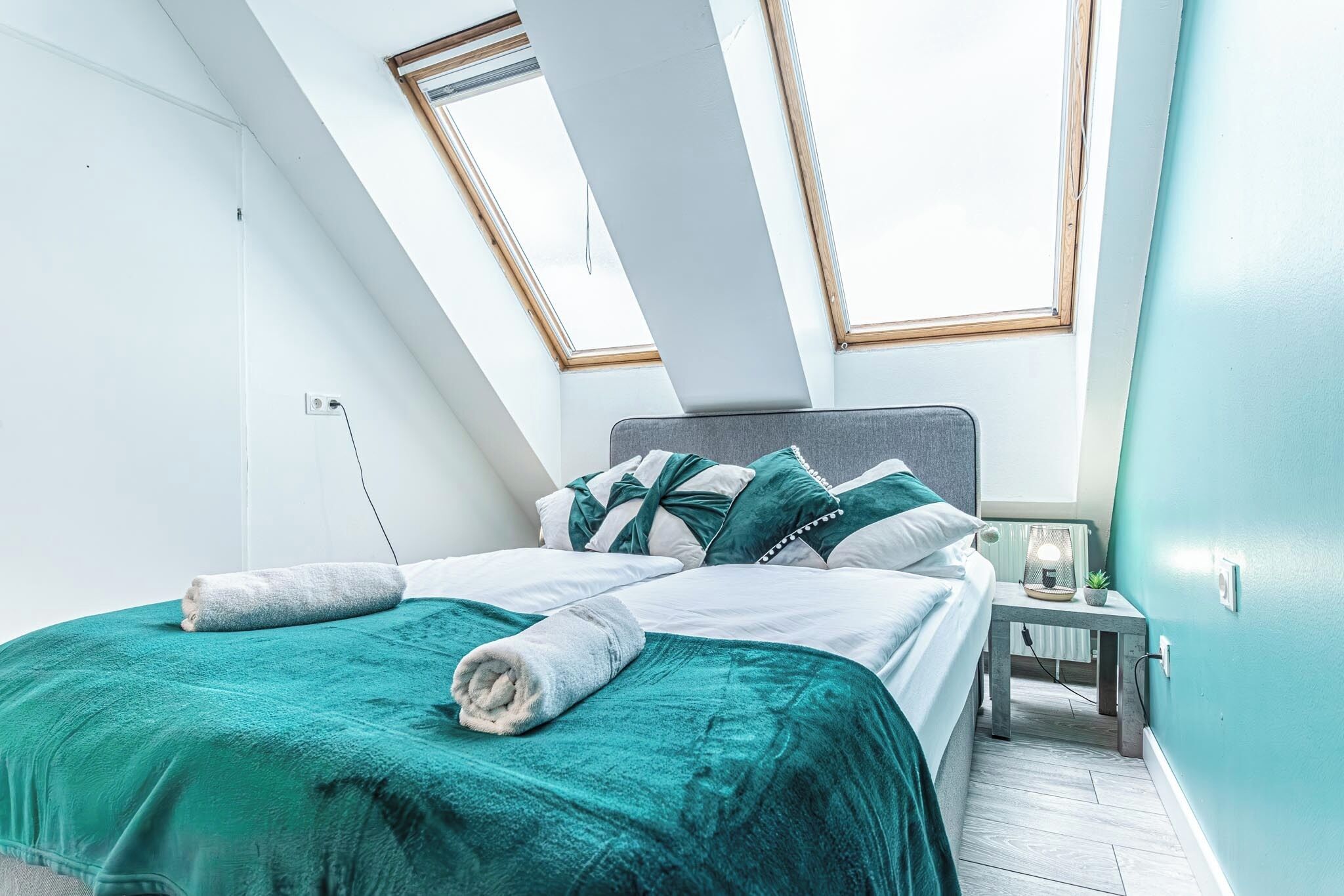 Un dormitorio con cama, mesita de noche, lámpara y ventana.