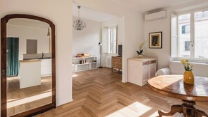 Una cucina moderna con mobili bianchi, pavimento in legno a spina di pesce e un tavolo rotondo in legno con un vaso di fiori.