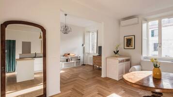 Una cucina moderna con mobili bianchi, pavimento in legno a spina di pesce e un tavolo rotondo in legno con un vaso di fiori.