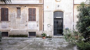 Un cortile con un edificio caratterizzato da una porta nera, una finestra rotonda e una pianta in vaso.