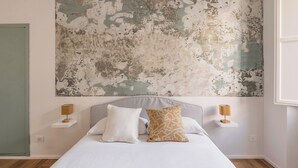 Una camera da letto con un grande quadro astratto appeso al muro, un letto con biancheria bianca, due comodini con lampade e una porta verde.
