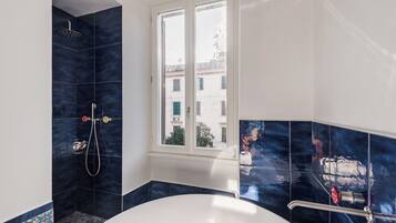 A modern bathroom with a bathtub, a shower, and a window providing a view of buildings outside.