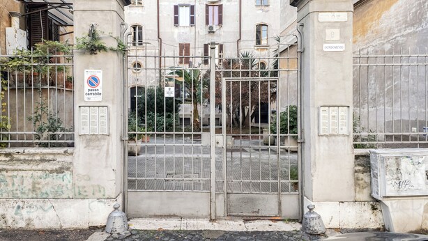 Un cancello chiuso conduce a un edificio, con un cartello che indica divieto di parcheggio.