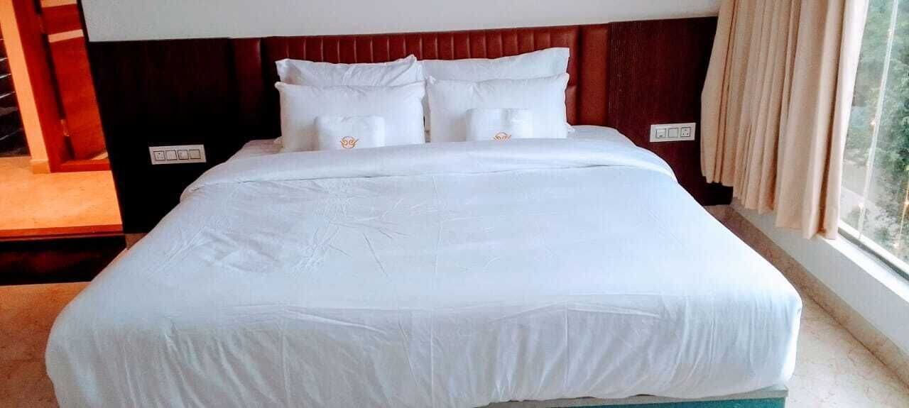 A large bed with white linens, a wooden headboard, and a window with curtains.