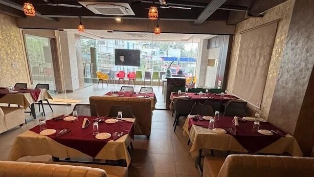 A restaurant with tables set for dining, a large TV screen, and a view of the street outside. - Hotel Amulya Royal Inn  (Bengaluru)