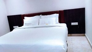 A neatly made bed with white linens in a room with white walls and a dark wood headboard. - Hotel Amulya Royal Inn  (Bengaluru)