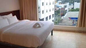 A hotel room with a large bed, a window with a view of buildings, and a curtain. - Hotel Amulya Royal Inn  (Bengaluru)