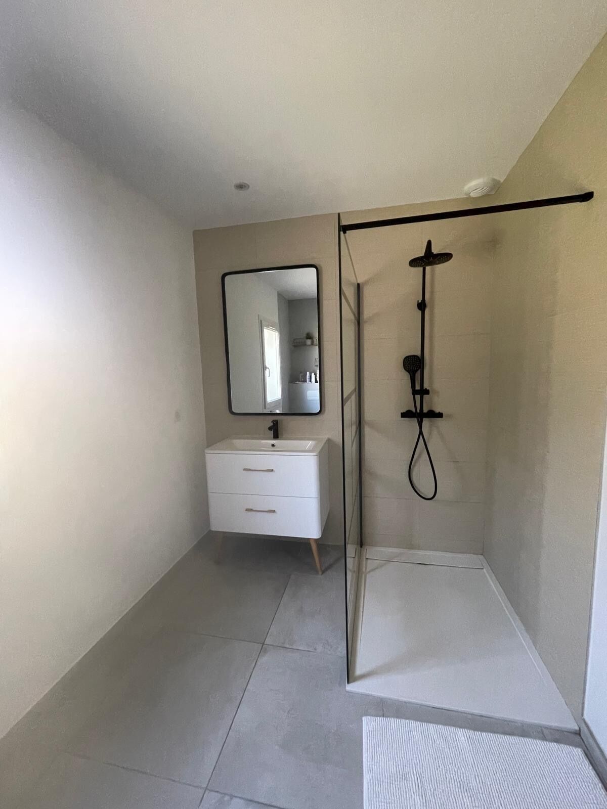Een moderne badkamer met een douchecabine van glas, een wit badkamermeubel met lades en een spiegel.