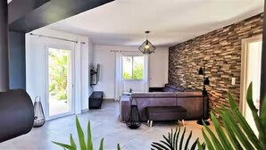 A modern living room with a stone wall, a sofa, and a large window. - Villa Premium à Saint-Raphaël - Heated pool, 6 suites and sea view (Saint-Raphaël)