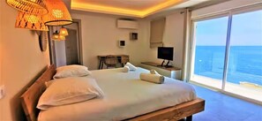 Quarto com cama grande, escrivaninha, cadeira, televisão e vista para o oceano.