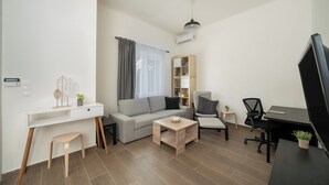 Un salon moderne avec un canapé, une table basse et un bureau avec une chaise. On y trouve également une bibliothèque, un petit tabouret et une plante en pot.