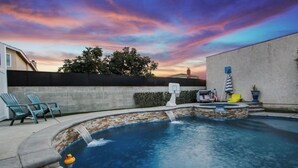 Un giardino con piscina, canestro da basket e una piccola cascata.