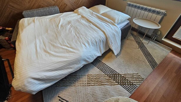 Ein modernes Schlafzimmer mit Fischgrätparkett, einem Bett mit weißer Bettwäsche, einem kleinen runden Tisch und einem Heizkörper.