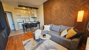 Ein modernes Wohnzimmer mit Sofa, Couchtisch und Essbereich mit Stühlen, im Hintergrund eine Küche.
