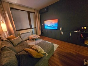 Un salon confortable avec un grand canapé, une petite table ronde et un téléviseur fixé au mur.