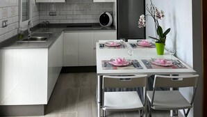 A modern kitchen with white cabinetry, a stainless steel refrigerator, and a dining area with a table set for two. - La Casita de La Pared: Ideal house for families, with game room. (LOS REALEJOS)