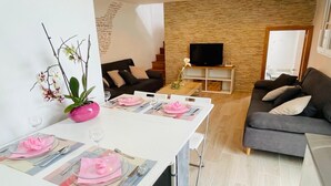 A modern living room with a grey sofa, a flat-screen TV on a wooden stand, and a dining area with a white table set for two. - La Casita de La Pared: Ideal house for families, with game room. (LOS REALEJOS)