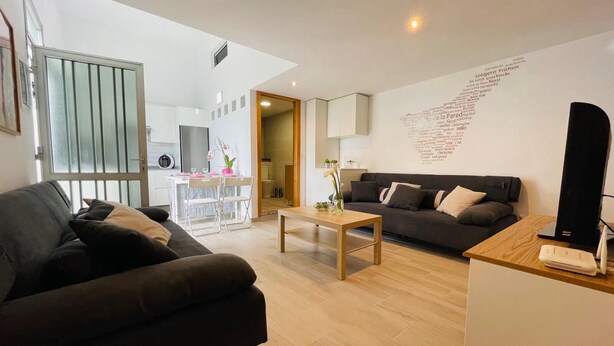 A modern living room with a sofa, a coffee table, and a TV stand. There is a dining area with a table and chairs in the background. - La Casita de La Pared: Ideal house for families, with game room. (LOS REALEJOS)