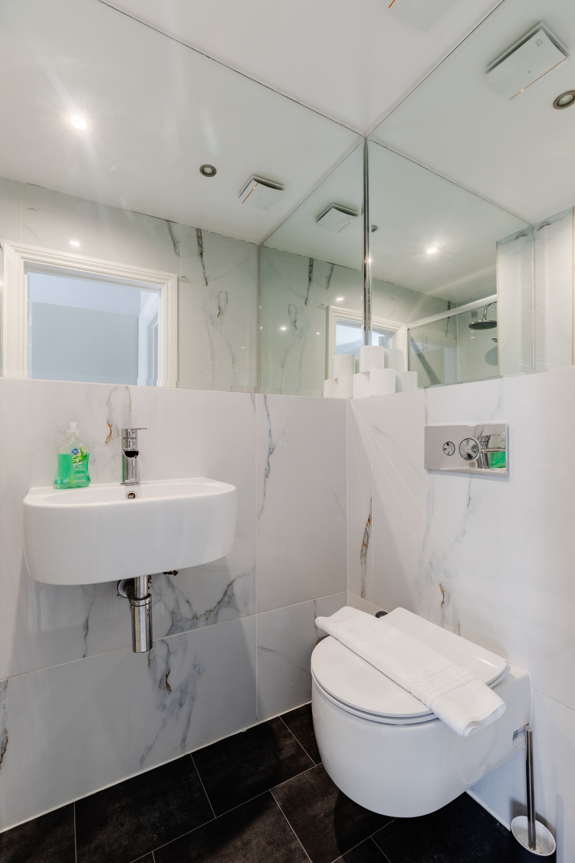 A modern bathroom with a white sink, marble walls, a toilet, and a glass shower enclosure.
