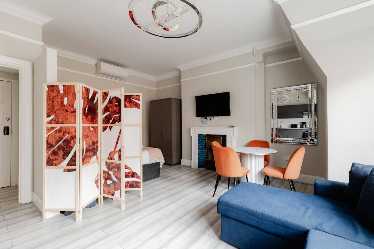 A modern living room with a blue sofa, orange chairs, a white fireplace, and a television mounted on the wall.