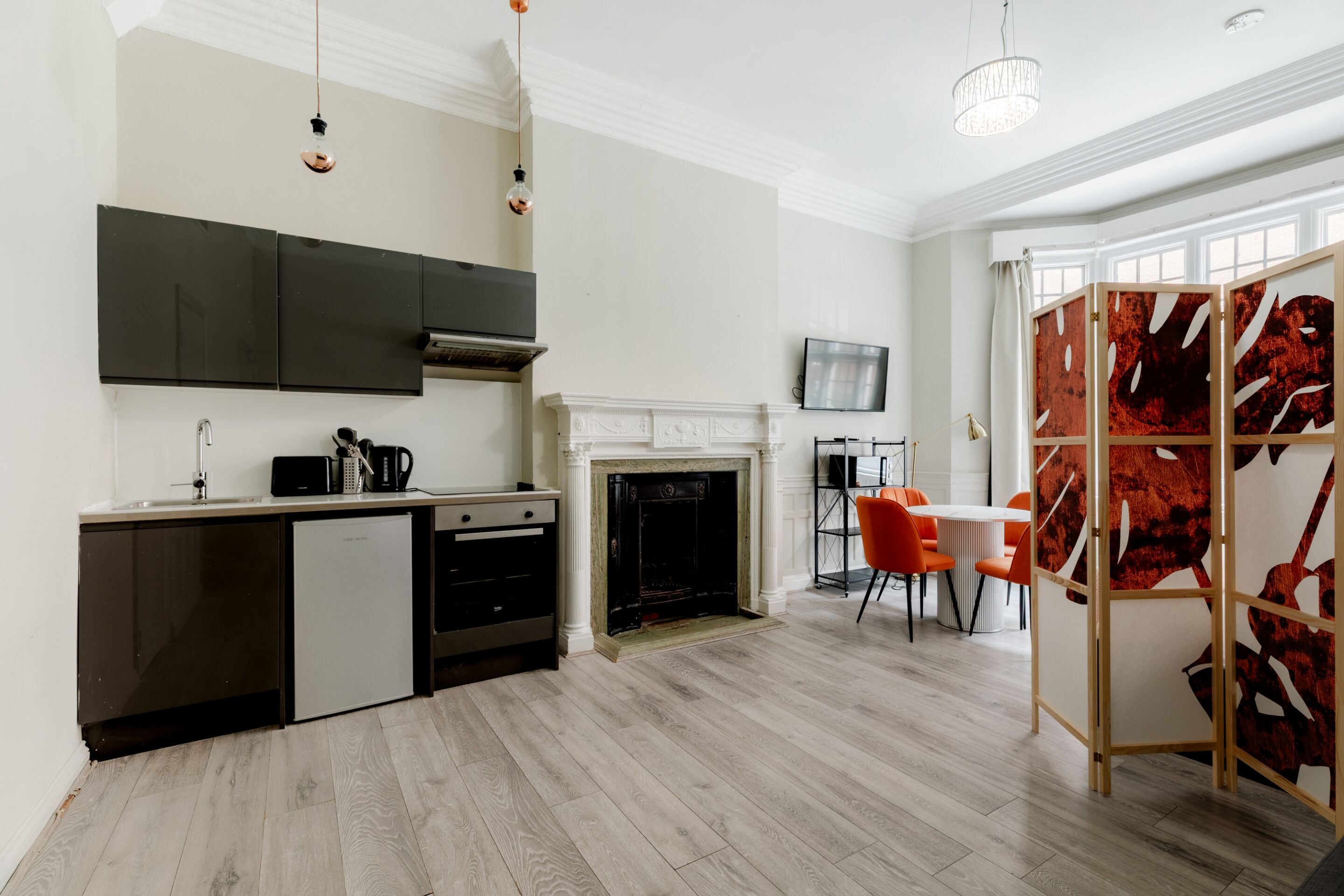 Una cocina moderna con lavavajillas integrado, chimenea y zona de comedor con sillas anaranjadas.